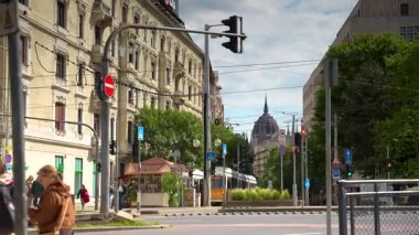Budapeşte, Macaristan - 17 Mayıs 2025: Budapeşte 'de eski binalar, yaya geçidi, şehir trafiği ve parlamento binasının uzak kubbesi ile güneşli bir kavşak.