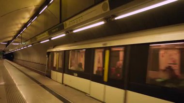 Budapeşte, Macaristan - 10 Kasım 2024: Pürüzsüz, modern bir beyaz tren Budapeşte 'deki Fovam ter metro istasyonuna ulaşır. Yeraltı platformunda sıcak sarı ışıklandırma ve kıvrımlı mimari duvarlar yer alıyor..