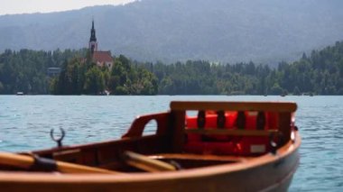 Bled, Slovenya - 11 Ağustos 2025: Geleneksel bir ahşap pletna tekne Bled Gölü 'nün sakin turkuaz sularında yüzüyor, arka planda ikonik ada kilisesi ve Alp ormanı var..