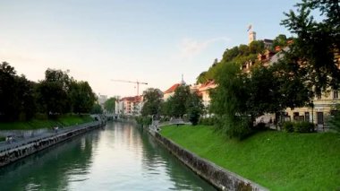 Ljubljana, Slovenya - 10 Ağustos 2025: Manzaralı bir manzara Ljubljanica Nehri 'nin Ljubljana' nın tarihi merkezinde dolanıp, yemyeşil setler ve zarif mimariyle kaplı olduğunu gösteriyor.