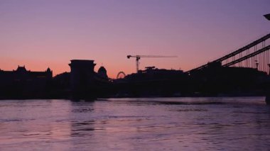 Budapeşte, Macaristan - 20 Eylül 2024: Tuna tufanı şehri sabahın erken saatlerinde yansıtırken Budapeşte üzerinde gün doğumu. Geçişi büyüt.