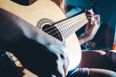 Kadın elleri akustik gitar çalıyor, yakın çekim.