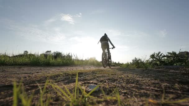 Uma jovem está andando de bicicleta até o pôr do sol no parque — Vídeo de Stock
