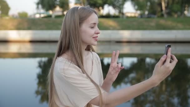 Mujer sentada en el parque y haciendo selfie, feliz. En el río — Vídeo de stock