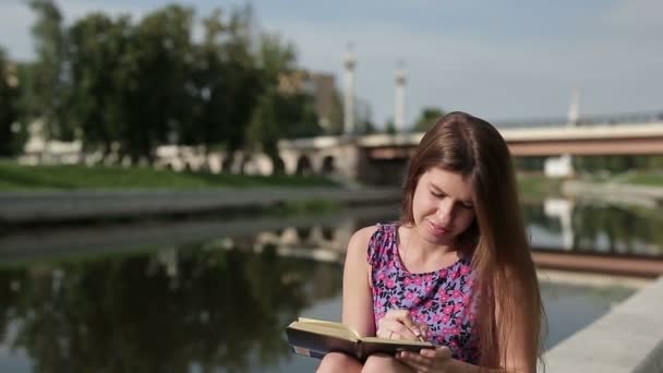 Wanita yang memegang jurnal dan menulis sesuatu sambil bersantai di taman — Stok Video