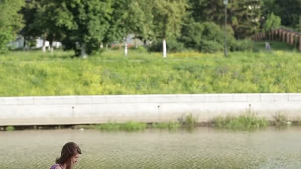 Νεαρή γυναίκα να γράψω κάτι στο σημειωματάριό της στην όχθη του ποταμού στο πάρκο της πόλης — Αρχείο Βίντεο