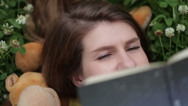 Jonge vrouw voor haar gezicht met een boek liggen op gras — Stockvideo