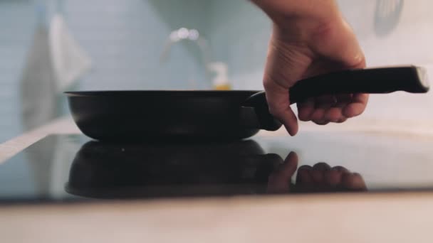 Рука людини кладе сковороду на індукційну варильну панель . — стокове відео