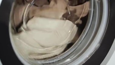 Çamaşır makinesi beyaz ve kahverengi giysileri yıkar.