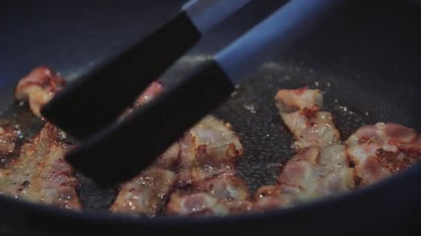 Kraftig og tynt bacon, røyker og koker i en varm, svart panne. – stockvideo