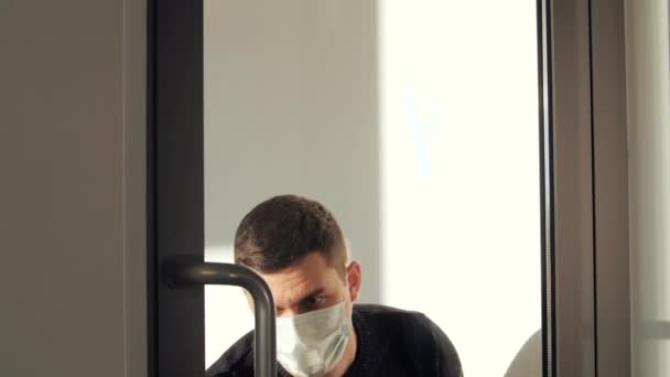 Hombre atractivo en máscara médica limpiando la puerta de cristal. Concepto de prevención de la propagación del virus. — Vídeos de Stock