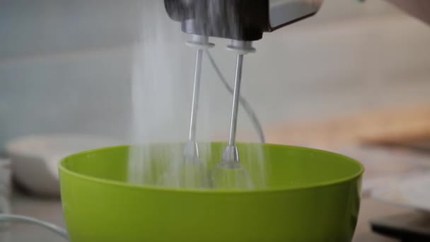 Close-up do chef peneira farinha para amassar a massa e chicoteá-lo com um misturador de mão em uma tigela verde. — Vídeo de Stock