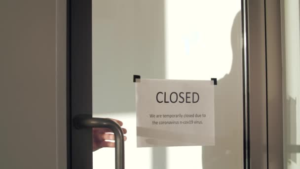 Ein gut aussehender, maskierter Mann geht zur Glastür und reißt das Schild "Geschlossen" herunter. Wiedereröffnung für Unternehmen Anpassung an neue Normalität in der neuen Coronavirus-COVID-19-Pandemie. — Stockvideo
