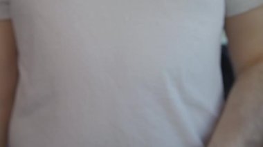 Beyaz tişörtlü beyaz bir adam fiziksel bir bitcoin ile elini kaldırır..