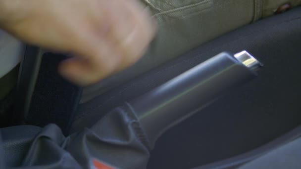 Рука водителя крупным планом поднимает рычаг тормоза и отстегивает ремень безопасности автомобиля. — стоковое видео