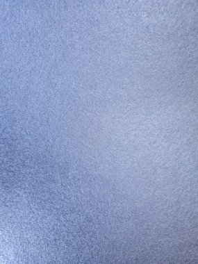 A macro photograph of a solid light blue surface with a grainy, textured finish. The subtle metallic sheen creates a gentle shimmer, offering a simple yet elegant abstract background for design projects, wallpaper, or creative concepts.