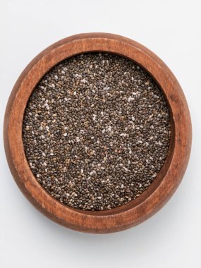 Top down view of raw, organic chia seeds in a round wooden bowl. The superfood ingredient is isolated on a clean white background, representing healthy eating, nutrition, diet, and vegan lifestyles.