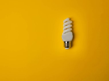 Top view of a single compact fluorescent spiral light bulb on a solid yellow background. This image represents concepts of energy conservation, sustainability, innovation, bright ideas, and modern technology. Ample copy space is available.