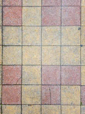 Top down view of an old pavement with a red and yellow checkered pattern. The square terrazzo tiles show signs of wear and age with visible cracks and dirt, creating a rustic and textured background for design projects.