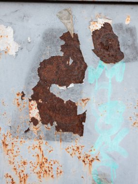 Yıpranmış metal bir duvarın detaylı yakın çekimi. Açık gri boya koyu pas lekelerini ortaya çıkarmak için soyuluyor. Açık mavi sprey boya graffitisi kirli ve çürümüş dokuya kentsel bir öğe ekler. Arka plan için mükemmel..