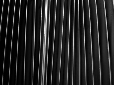 A striking black and white close-up of vertical metal fins. The dramatic play of light and shadow creates a strong, rhythmic pattern, perfect for an abstract, industrial, or modern technology background evoking structure and precision.