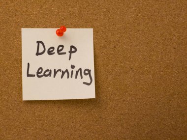 Derin öğrenme kelimeleri beyaz yapışkan bir nota el yazısıyla yazılmış. Not, yapay zeka, makine öğrenme ve modern teknoloji kavramlarını temsil eden kahverengi bir mantar panoya kırmızı bir iğneyle tutturulmuştur..