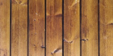 A close-up view of a natural wood surface with vertical planks. The rich brown texture features visible grain and knots, creating a rustic and warm background for design projects or wallpaper.