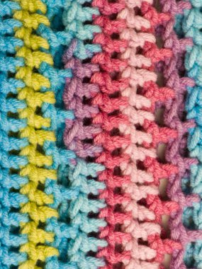 El yapımı tığ işi bir kumaşın aşırı yakın çekimi. Tekstil, mavi, sarı, pembe ve mor tonlarında parlak pastel ipliğin dikey çizgilerine sahiptir. Açılış dikişi, arka plan için mükemmel yumuşak, rahat bir doku yaratır..