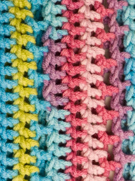 El yapımı tığ işi bir kumaşın aşırı yakın çekimi. Tekstil, mavi, sarı, pembe ve mor tonlarında parlak pastel ipliğin dikey çizgilerine sahiptir. Açılış dikişi, arka plan için mükemmel yumuşak, rahat bir doku yaratır..