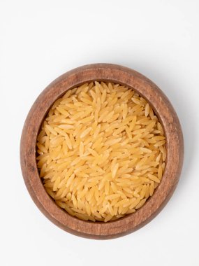 Top view of uncooked orzo, also known as risoni, in a rustic wooden bowl. The small, rice-shaped pasta is a staple ingredient in Italian and Mediterranean cuisine, shown here isolated on a clean white background with copy space.