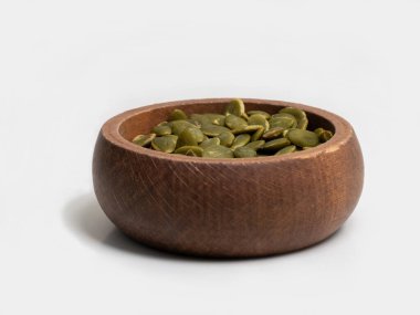 A close-up of raw green pumpkin seeds, also known as pepitas, in a small wooden bowl. This healthy snack and superfood ingredient is isolated on a clean white background, perfect for nutrition and diet concepts.
