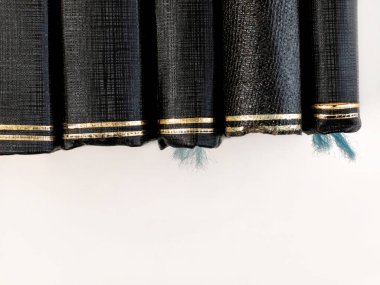 Eski, iyi okunmuş kitapların diplerine yakından bakmak. Siyah kapaklar zarif altın folyo şeritleriyle desen ve yaşı gösteriyor. Aşınmış mavi iplikler yıpranmış kenarlardan asılı, kopyalama alanı olan temiz beyaz arkaplana karşı.