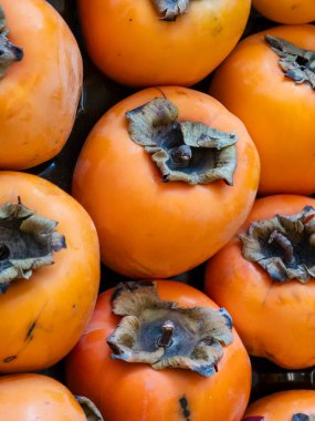 Canlı, tepeden tırnağa taze, olgun portakal hurmaları. Kurumuş kalsiyumlarıyla parlak meyveler yiyecek, sağlık ve mevsimsel sonbahar hasat kavramları için mükemmel doğal bir arka plan oluşturur ve meyvelerin dokusunu gösterir..