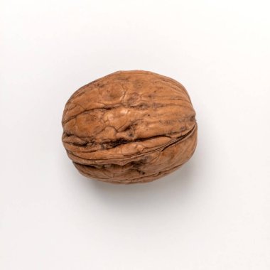 Temiz beyaz arka planda, kabuğunda tek bir ceviz kabuğunun üst görüntüsü. Görüntü fındığın doğal kahverengi rengini ve buruşuk dokusunu vurguluyor, sağlıklı beslenme, organik gıda ve doğal bileşenleri temsil ediyor..