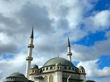 Türkiye 'nin İstanbul kentinde etkileyici kubbeleri ve yükselen mineralleriyle büyük bir camiinin çarpıcı manzarası. İslam mimarisi, inanç ve kültürü sembolize eden beyaz bulutlarla dolu dinamik mavi bir gökyüzüne karşı duruyor..