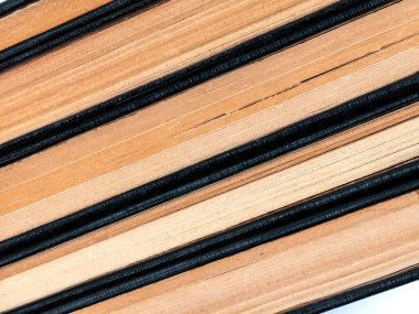 Eski bir kitap yığınının yakın plan, soyut bir görüntüsü. Sarı kağıt sayfalar ve koyu dokulu dikenler, tekrar eden çapraz desenler yaratır, edebiyat, eğitim, tarih ve bilgi ile ilgili arka planlar için mükemmeldir..