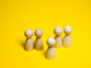 Bir grup basit tahta bebek figürleri, parlak sarı bir arka plana yerleştirilmiş. Bir figür liderliği, halk konuşmasını veya bireyselliği temsil ederken, diğerleri bir takımı, kalabalığı veya toplumu temsil ediyor. Yönetim ve birlik.
