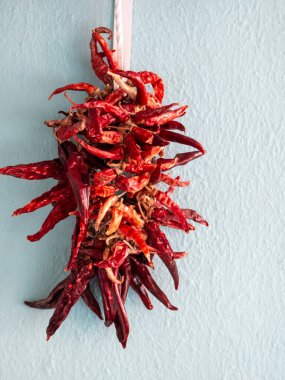 Ristra olarak bilinen canlı kırmızı kırmızı biber demeti soluk mavi bir duvara asılır. Bu geleneksel kurutma metodu aynı zamanda kırsal bir dekorasyon, hasat ve baharatlı mutfağı sembolize eder..