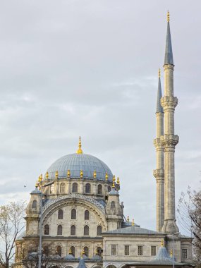 Görkemli tarihi bir caminin mimari manzarasında altın kaplamalı büyük bir merkez kubbe ve iki uzun ince minare bulunur. Karmaşık taş mimarisi, İstanbul 'da bulutlu bir gökyüzü altında klasik Osmanlı tarzını yansıtıyor.