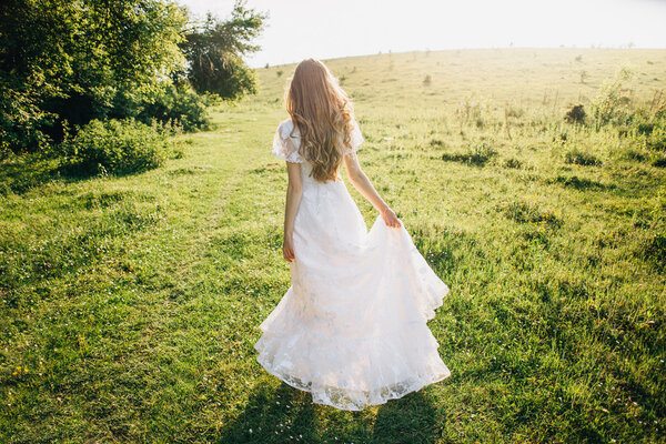 Young girl in a beautiful long white dress walking in the meadow