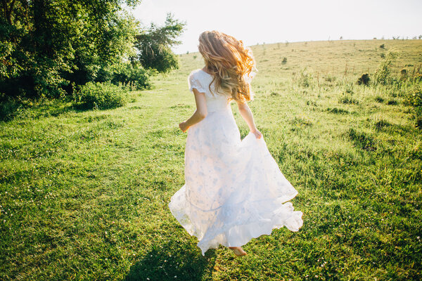 Young girl in a beautiful long white dress running in the meadow