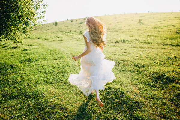Young girl in a beautiful long white dress running in the meadow