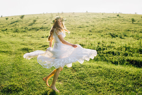 Young girl in a beautiful long white dress dancing in the meadow