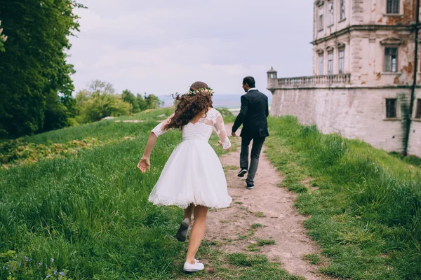 Newlyweds running by old castle — Stock Photo, Image