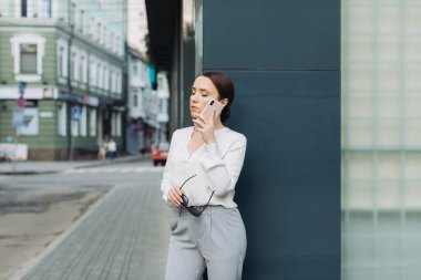 Caddede yürürken gülümseyen genç bir iş kadınının cep telefonunu kullanması..