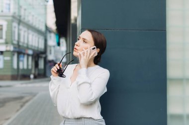 Caddede yürürken gülümseyen genç bir iş kadınının cep telefonunu kullanması..