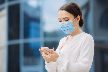 Koruyucu maskeli bir iş kadını telefonunu kontrol ediyor.