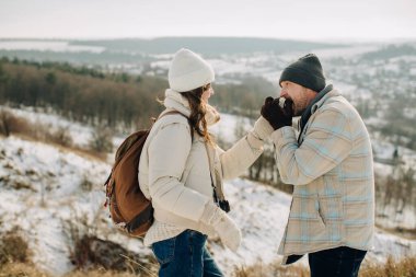 Baba kızlarının ellerini, karlı bir tepede nefesiyle ısıtıyor. Açık havada, iç açıcı bir aile anının tadını çıkarıyor.