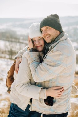 Dad and young smiling daughter warmly hugging outdoors in a cold winter landscape, showing family love