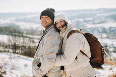 Baba ve kızı kışlık kıyafetler giyiyor, kucaklaşıyor ve gülümsüyor, kış manzarasında mutlu bir anı paylaşıyorlar.